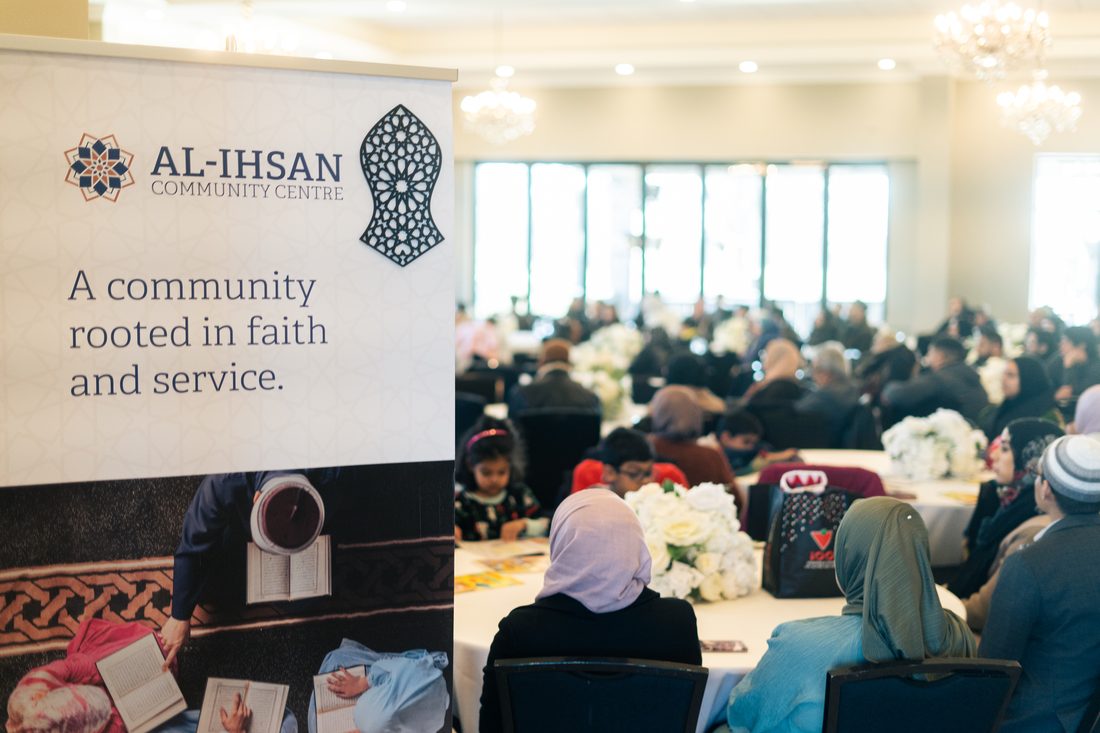 Families seated at a community fundraiser dinner beside an Al-Ihsan banner
